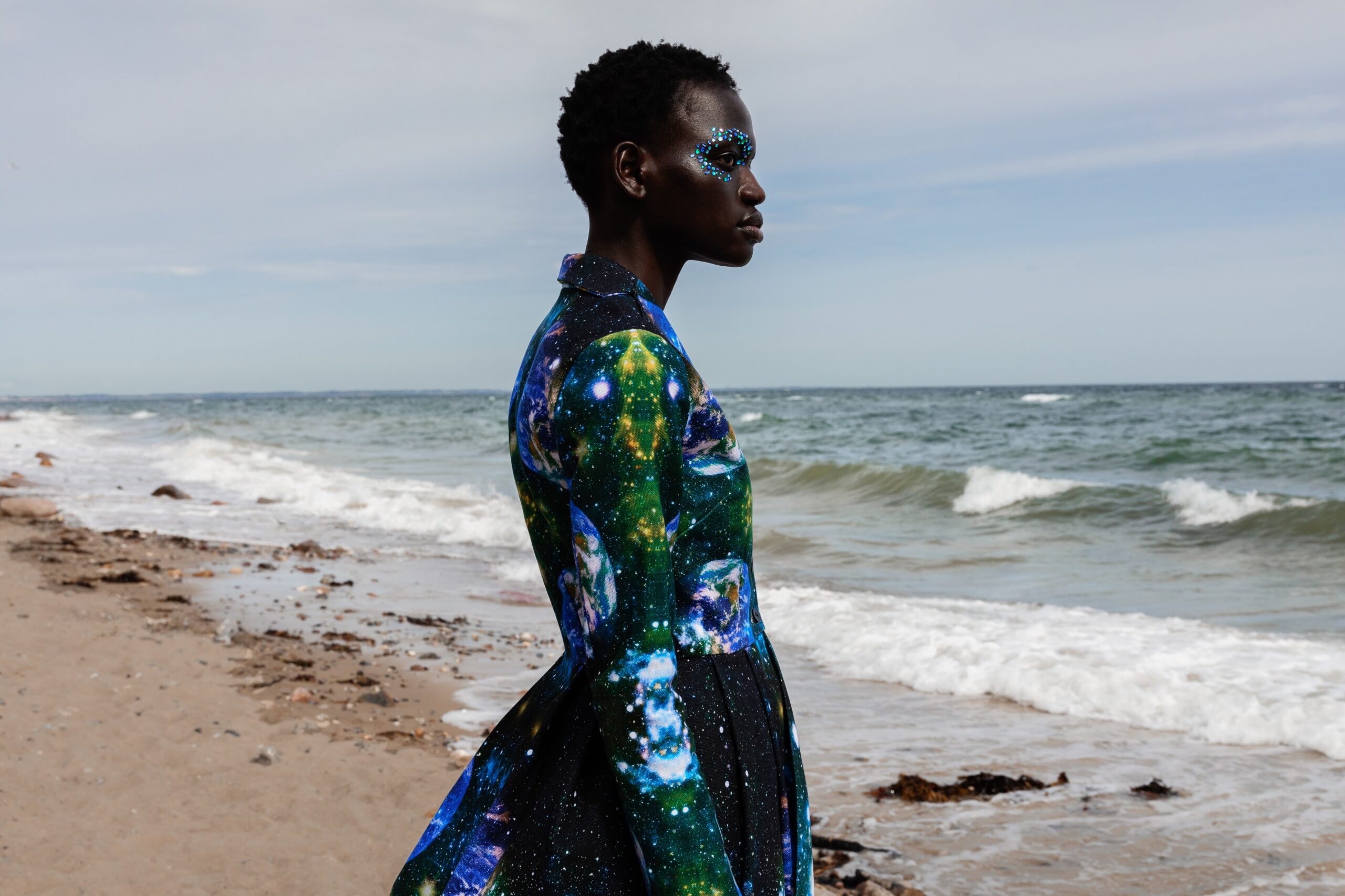 Farbige Frau steht im Kleid am Strand mit Glitzer Make up