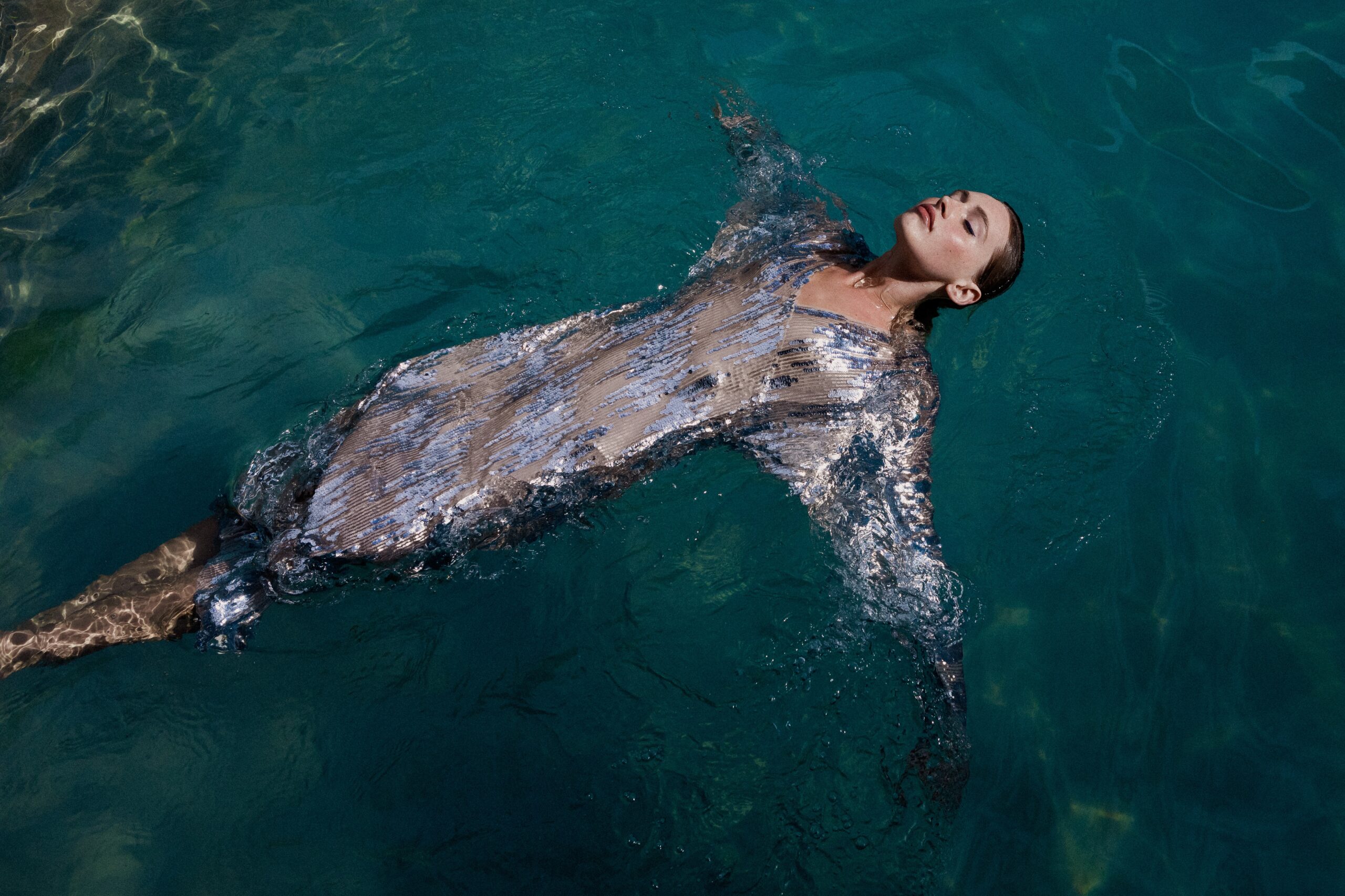 Eine Frau liegt im Pool mit Pailettenkleid